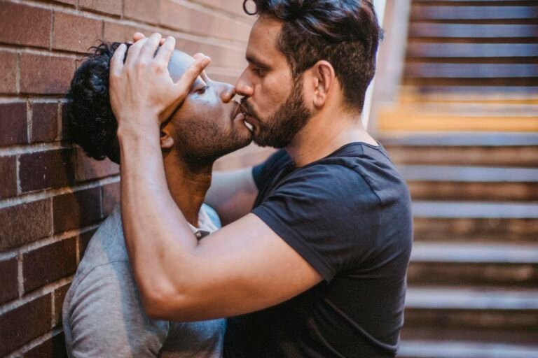 An interracial couple intimately kissing against a brick wall near stairs, expressing love and romance.